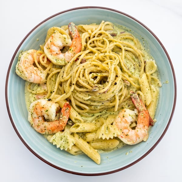 Creamy herb pasta with spaghetti, penne, bow-tie pasta, and shrimp served in a blue bowl.