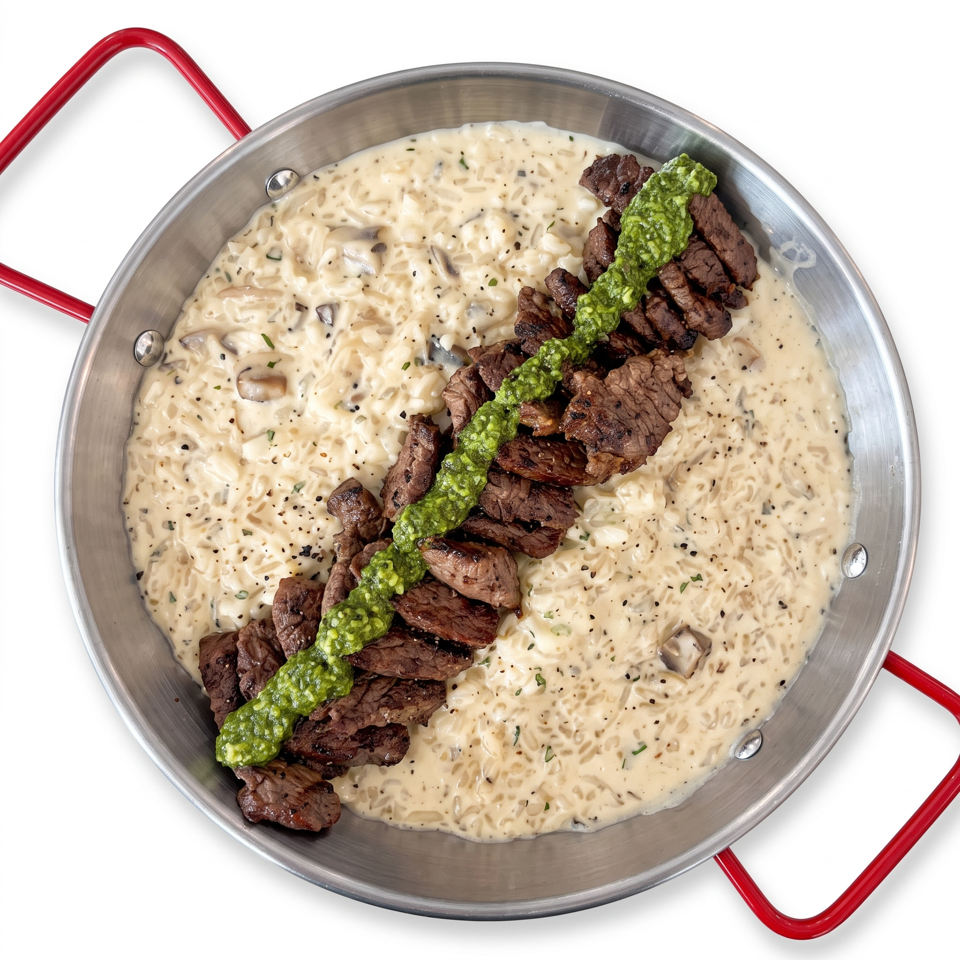 Grilled beef strips topped with green sauce over creamy mushroom rice in a metal skillet with red handles.